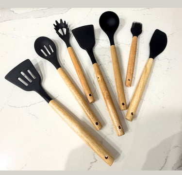 Set of kitchen utensils with black ends and wooden handles on a white marble surface